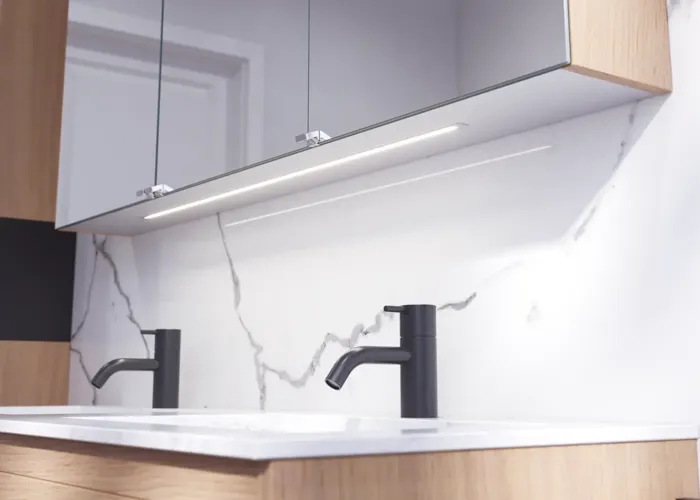 Badezimmerinspiration mit hellen Eichenmöbeln mit Lamellen, elegantem Doppelwaschbecken, schönem Spiegelschrank mit Licht, Fischgrätboden und weißer Marmorwand für ein klassisches, helles Aussehen.