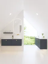Elegante und moderne Badezimmer Inspiration mit schrägem Dach, wandmontierten blauen Waschtischunterschränken und Unterschränken, rundem Waschbecken mit Messingarmatur, beleuchtetem Spiegel und natürlichem Licht
