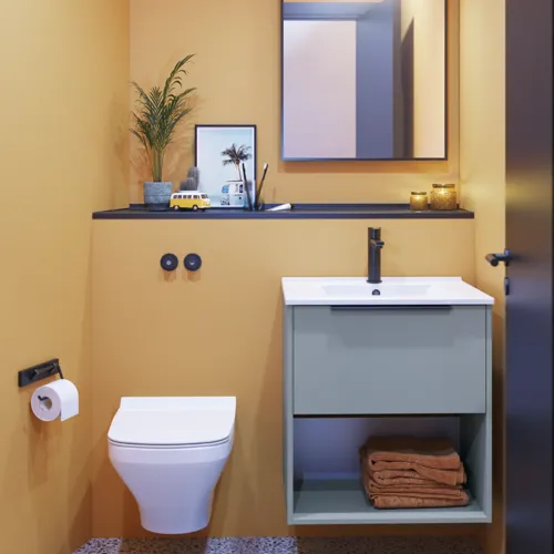 Kleine Badezimmerinspiration mit schrägen und warmen gelben Wänden, elegantem hellblauem Waschtisch, dünnem und stilvollem Waschbecken sowie minimalistischem quadratischem Spiegel mit schwarzem Rand und praktischer Lampe.