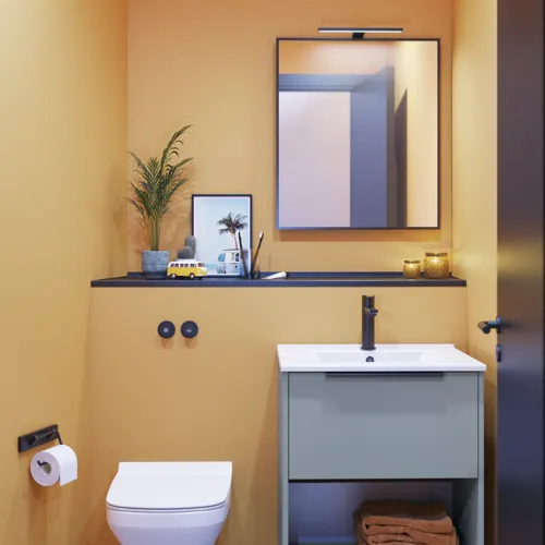 Kleine Badezimmerinspiration mit schrägen und warmen gelben Wänden, elegantem hellblauem Waschtisch, dünnem und stilvollem Waschbecken sowie minimalistischem quadratischem Spiegel mit schwarzem Rand und praktischer Lampe.