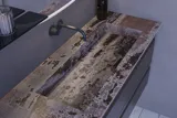 Inspiration für ein großes Badezimmer mit grauem Waschtischunterschrank mit integriertem Griff, stilvollem, seitlich montiertem Waschbecken, quadratischem Spiegel mit abgerundeten Ecken, Wänden in Betonoptik und rohen Materialien für einen urbanen Look