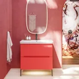 Badezimmer-Inspiration mit roten Wänden, sanft geformtem roten Waschtischunterschrank und Hochschrank, elegantem weißen Waschbecken und schönem ovalem Spiegel mit Beleuchtung, die zusammen mit der natürlichen Umgebung ein Vintage-Flair schaffen